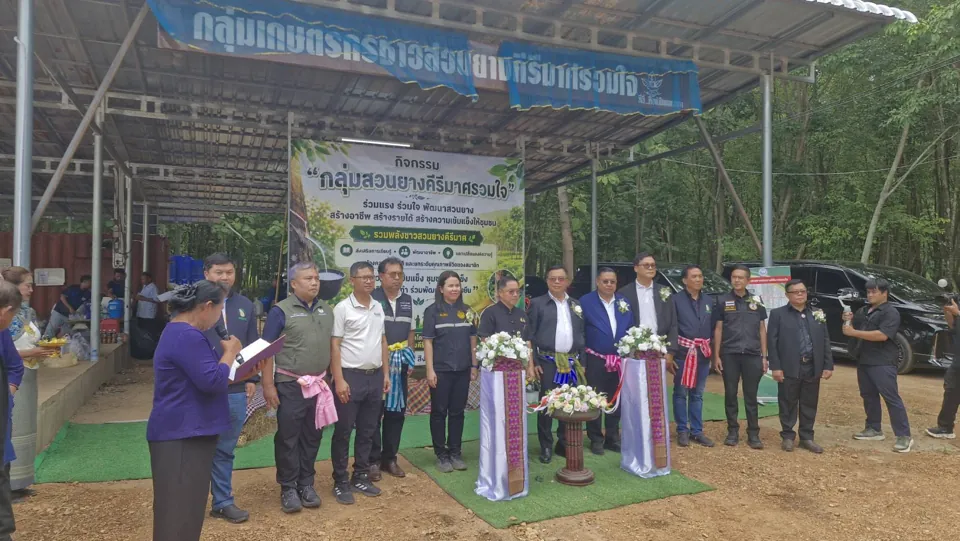 พิธีเปิดกิจกรรมใต้ป้ายกลุ่มเกษตรกรชาวสวนยางคีรีมาศรวมใจ มีแขกผู้มีเกียรติยืนเรียงแถวหน้าป้ายงาน